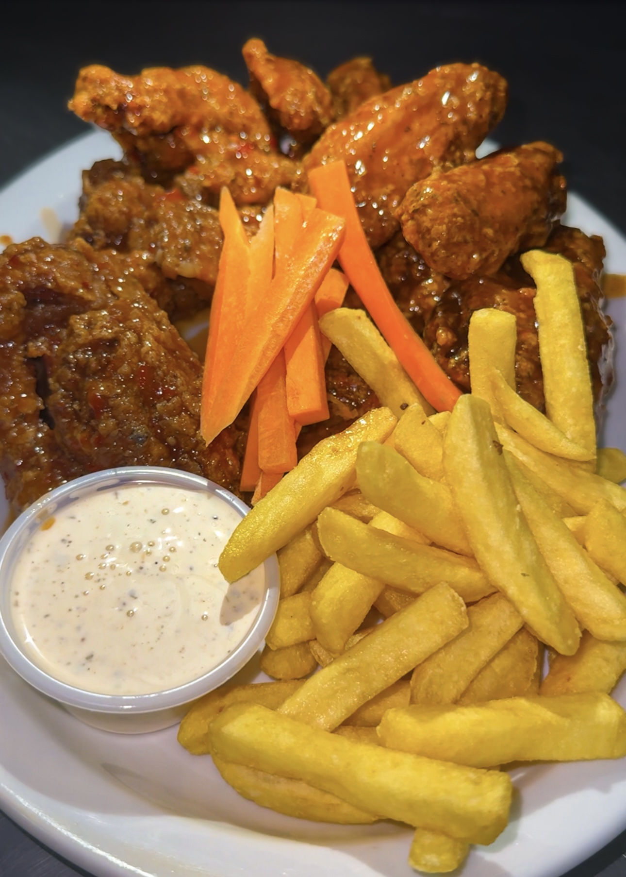 Alitas de pollo con papas fritas, bastones de zanahoria y dip ranch.