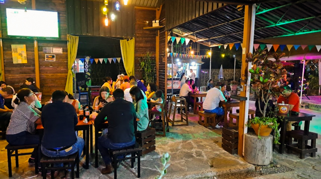 Comedor techado con invitados disfrutando la noche, banderines de colores y luces cálidas.