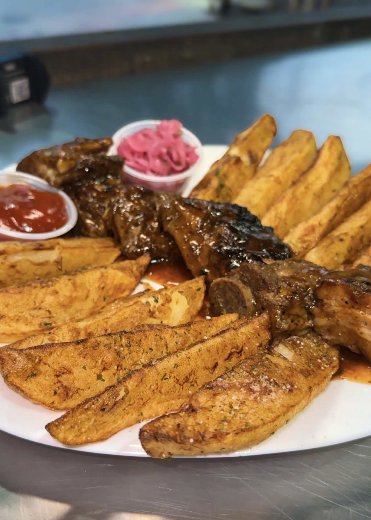 Plato de costillas glaseadas con papas rústicas y cebolla encurtida.