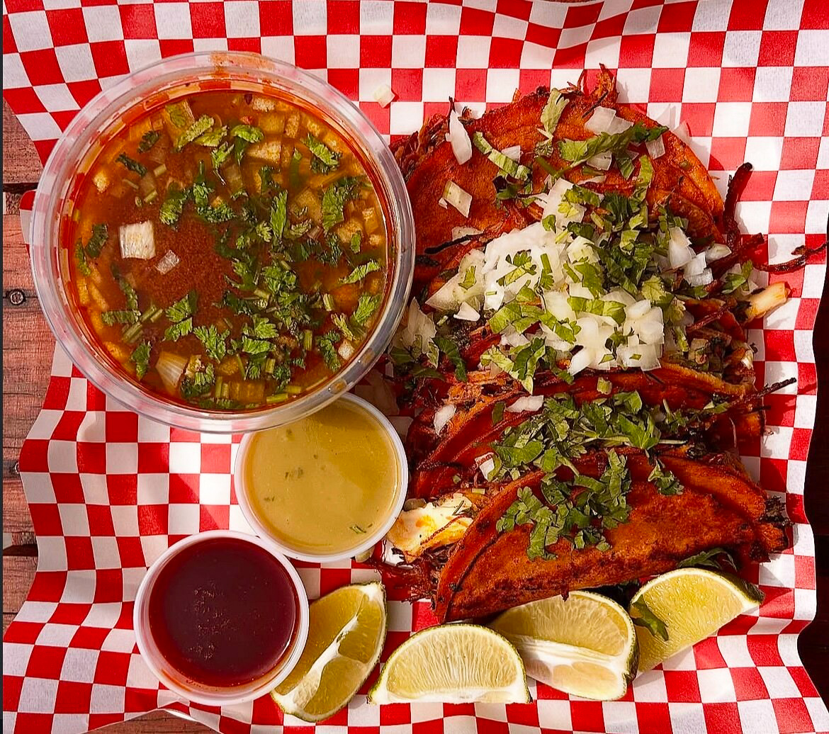 Tacos de birria con consomé, limones y salsas.