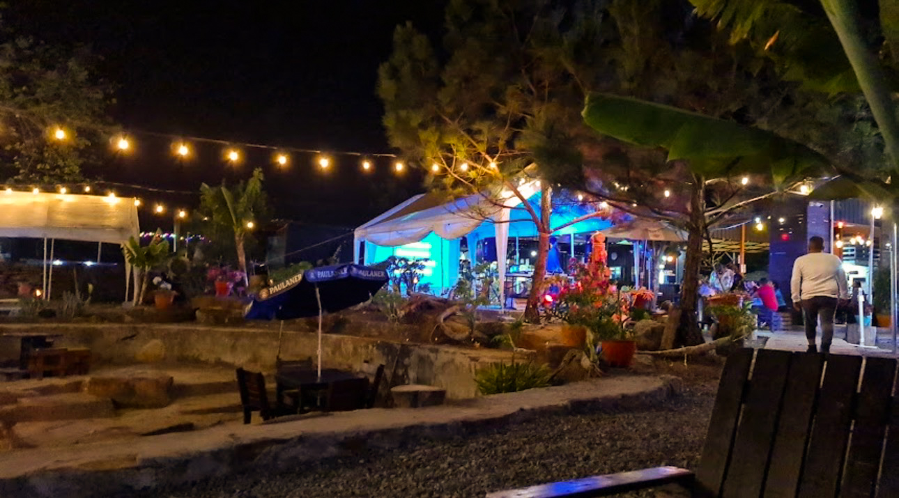 Vista panorámica nocturna de la terraza con luces de cadena, sombrillas y ambiente azul neón.